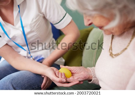 Female Physiotherapist Getting Senior Woman To Squeeze Rubber Ball At Home