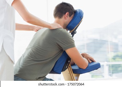Female physiotherapist giving shoulder massage to man on massage chair in hospital