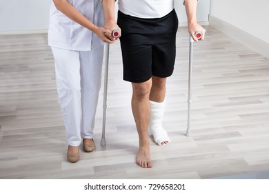 Female Physiotherapist Helping Injured Man To Walk With Crutches In Hospital - Powered by Shutterstock