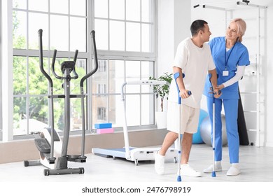 Female physiotherapist and young man with crutches walking in rehabilitation center