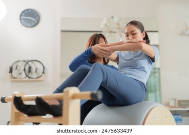 Female pilates trainer working out on pilates machine in studio Young woman stretching and pilates instructor holding her gently Pilates instructor helping a student with exercises class - Powered by Shutterstock