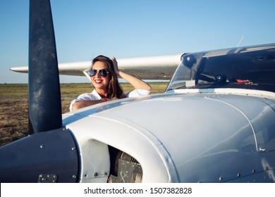 Female pilot in sunglasses with modern small aircraft in background.
