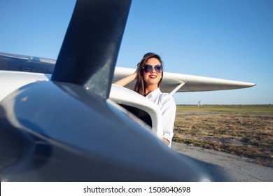 Female Pilot In Sunglasses With Modern Small Aircraft In Background.