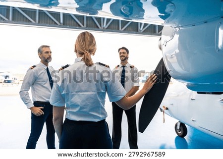 Female pilot touching propeller while discussing flight plans and aviation with two male pilots standing in a professional hangar setting, representing teamwork and training