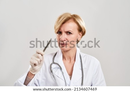 Female plastic surgeon with scalpel look at camera. Caucasian woman with stethoscope wear white coat and latex glove. Medical and health care. Plastic surgery. White background in studio. Copy space