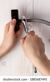 Female Plumber Connecting Flexible Hose To Black Water Stopcock. On White Wooden Background.