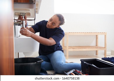 Female Plumber Working To Fix Leaking Sink In Home Bathroom