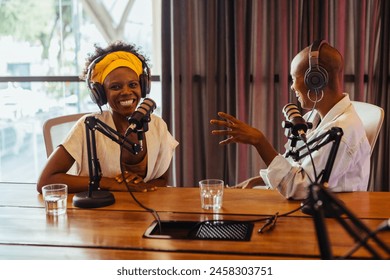 Female podcast hosts engaging in a dialogue filled with genuine laughter. Two black women recording a broadcast session in a studio equipped with professional microphones and headphones. - Powered by Shutterstock