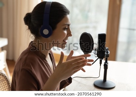 Female podcaster sit at table speaking into microphone stand on tripod talk speech share information, make audio podcast for internet audience, close up. Streaming, online radio program event concept