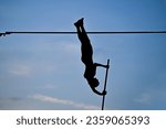 A female pole vaulter (body silhouette) jumping with a beautiful blue sky in the background. Track and field athlete. Woman pole-vaulting. Pole vault competition