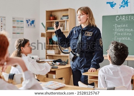 Female police office standing in classroom showing transmitter device to group of kids on career day at school
