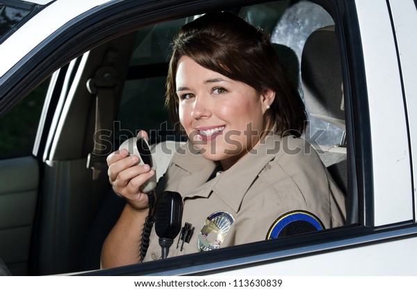 a female police officer smiles while sitting in her\
patrol car.