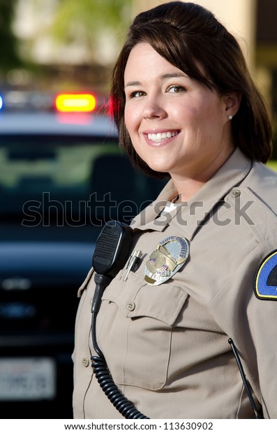 a female police officer smiles while standing in\
front of her patrol car.