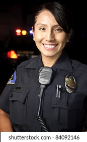 a female police officer smiling at night with her patrol car in the background.