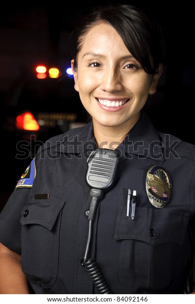 a female police officer smiling at night with\
her patrol car in the\
background.