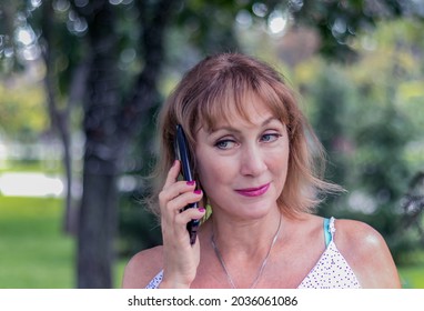 Female Portrait, Beautiful Mature Woman With Blond Hair, With A Sly Smile, Calls On A Mobile Phone