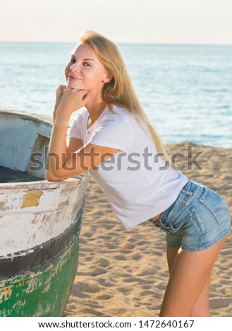 Female is posing on beach near boat in her free time near ocean.