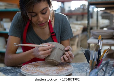 Female potter carving mug in pottery workshop - Powered by Shutterstock