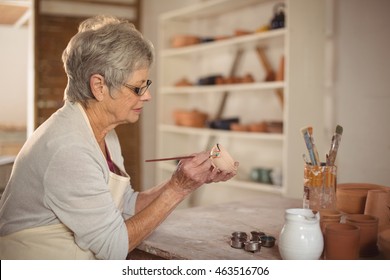 Female potter painting on bowl in pottery workshop - Powered by Shutterstock