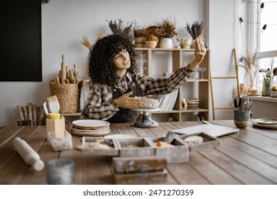 Female potter recording vlog in a cozy studio while sculpting clay. She is sharing her pottery skills and insights with her audience. - Powered by Shutterstock