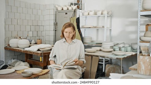 Female Potter Reviewing Notes in Busy Pottery Studio - Powered by Shutterstock