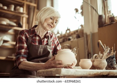 Female potter sitting at table and examining ceramic bowl at workshop - Powered by Shutterstock