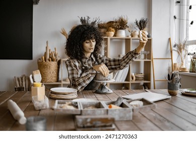 Female potter taking selfie in studio surrounded by ceramics tools and creations, showcasing her work and process for social media. - Powered by Shutterstock