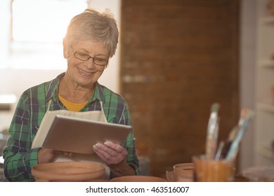 Female potter using digital tablet in pottery workshop