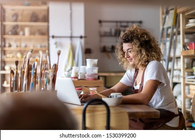 Female Potter Using Laptop In Art Studio 