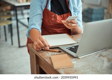 Female potter using mobile phone and laptop in workshop - Powered by Shutterstock