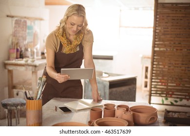 Female potter using mobile phone while working in pottery workshop - Powered by Shutterstock