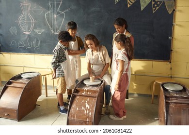 Female Potter Using Wheel While Showing How To Make Clay Vase To Kids At Pottery Class