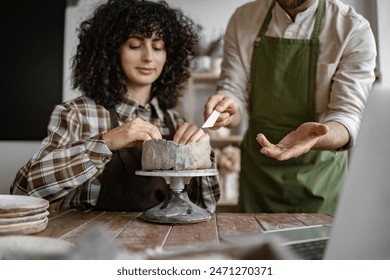 Female pottery student learning ceramic techniques from male instructor in craft studio. Hands-on pottery lesson and creative workshop. - Powered by Shutterstock