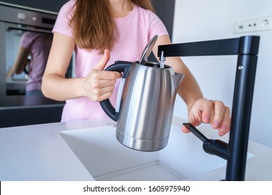 Female Pours Fresh Clean Filtered Purified Water From A Tap Into An Electric Kettle For Boiling Water At Kitchen At Home