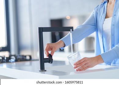 Female Pours Fresh Filtered Purified Water From A Tap Into A Glass At Kitchen At Home