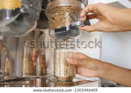 Female Pours Green Lentils from Vending Machine in a Glass Jar. Young Vegan Woman Shopping at Zero Waste Shop. No plastic Conscious Minimalism Lifestyle Concept.