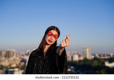 Female power, women rights, activism concept. Portrait of brunette superhero girl in black dress and red face mask showing korean heart at urban city background. Protesting for freedom and equality - Powered by Shutterstock