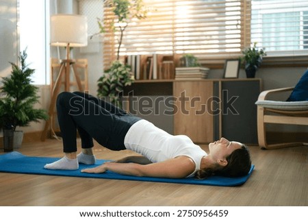 Female practicing glute bridge exercise on yoga mat indoors.