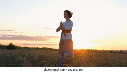 Female practicing qigong in summer fields with beautiful sunset on background	