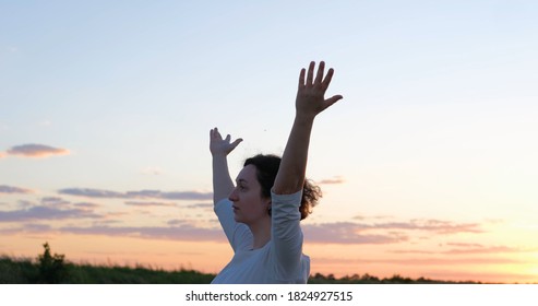 Female practicing qigong in summer fields with beautiful sunset on background	
