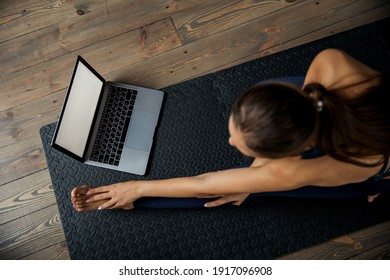 Female practicing yoga or pilates indoors on mat, doing exercises and stretching, watching video lesson online. Top view - Shutterstock ID 1917096908