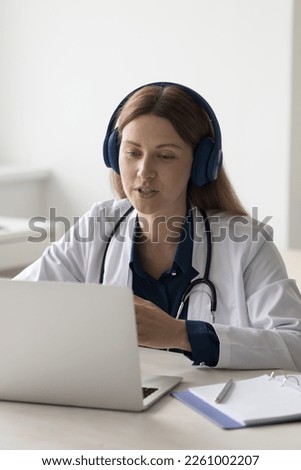 Female practitioner giving online consultation, advice, help to patient, using wireless headphones, laptop computer for remote communication, speaking on video call, medical conference