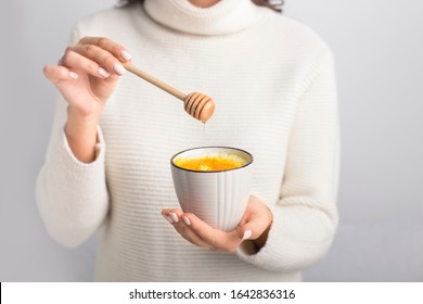 Female Preparing Turmeric Latte Drink With Honey On Gray Background. Cup With Yellow Milk. Detox Curcumin Drink