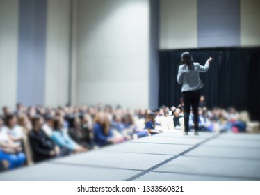 Female Presenter And Audience During Presentation.
Blurred Female Speaker Photo At Conference Meeting. Woman Presenter On Stage At Business Seminar. Lecturer Giving Speech. People Attend Presentation.