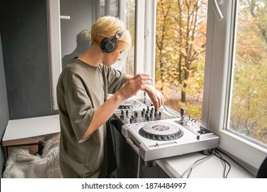 Female pretty blonde DJ, producer, composer enjoying mixing music in home recording studio while working near the open window. Music production and broadcasting concept