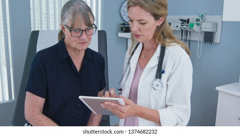 Female Primary Care Physician Having Conversation With Older Caucasian Woman During Regular Check Up. Senior Patient Talking With Her Reassuring Doctor In Exam Room