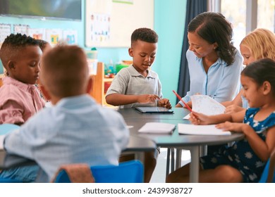 Female Primary Or Elementary School Teacher Helping Students With Digital Tablet At Table In Class - Powered by Shutterstock