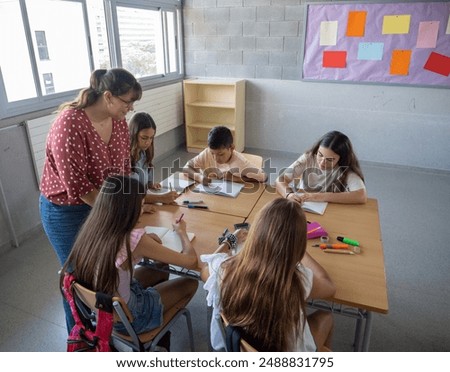 Female primary school teacher explaining in class to a group of students sitting at desks. Back to school