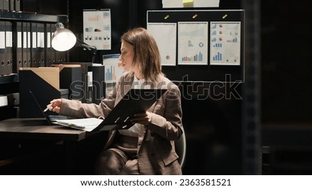Female private detective enters office space reviewing evidence and conducting thorough investigation using laptop. Filled with files and folders room is equipped with technology for crime analysis.
