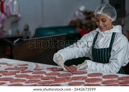 Female processing operator arranging burger patties on stainless steel table in plant, copy space. Industrial, manufacturing, hygiene, cleanliness, precision, automation, efficiency